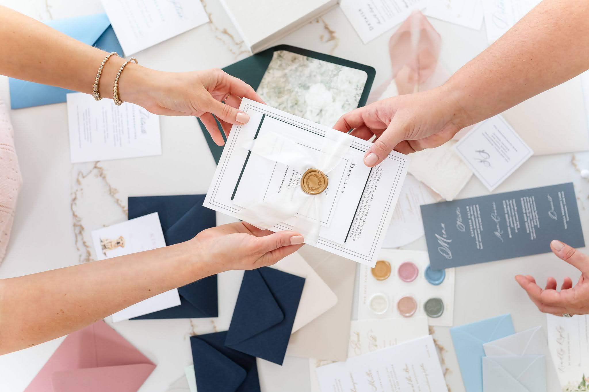 Two wedding stationers hold an invitation suite with ribbon and wax seal