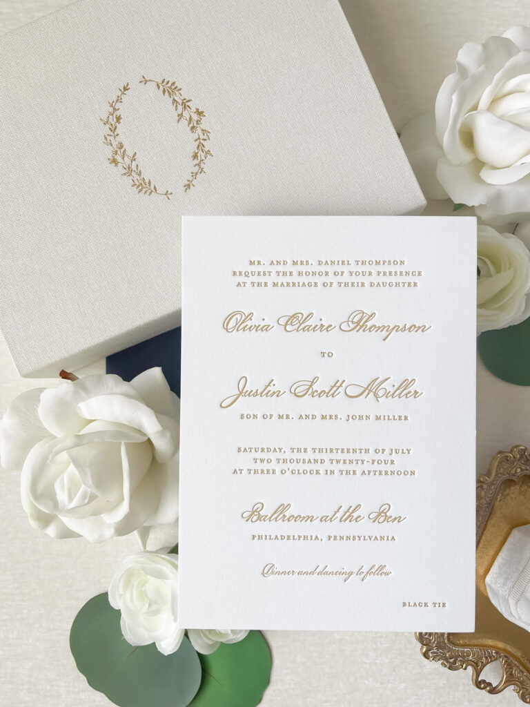 Custom gold letterpress invitation resting on linen keepsake box