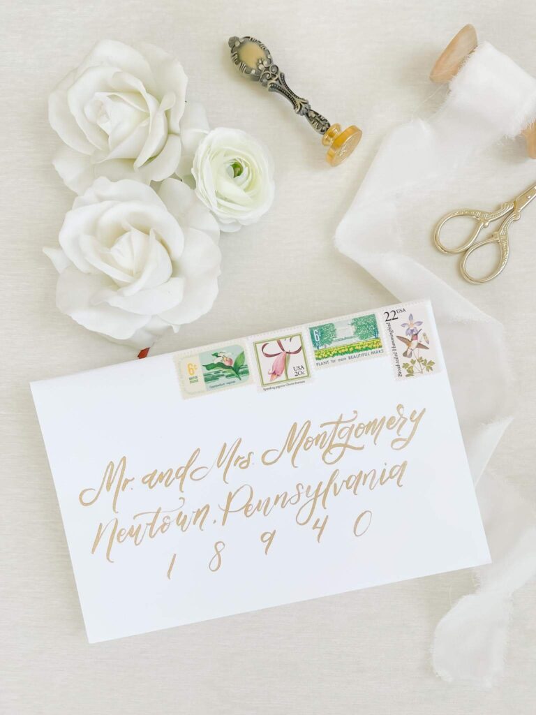 White wedding envelope with elegant gold calligraphy and vintage postage