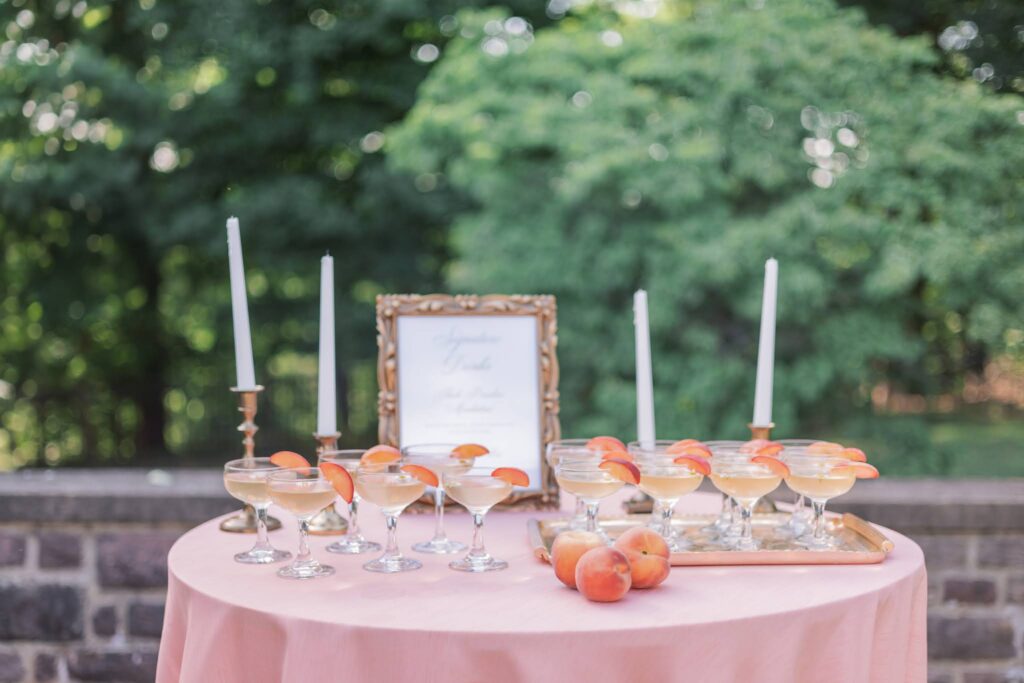 Drink table at summer garden wedding at Tyler Gardens. Pink tablecloth, peach drinks, and plenty of fresh peaches are featured as part of Pantone's color of the year, "Peach Fuzz."