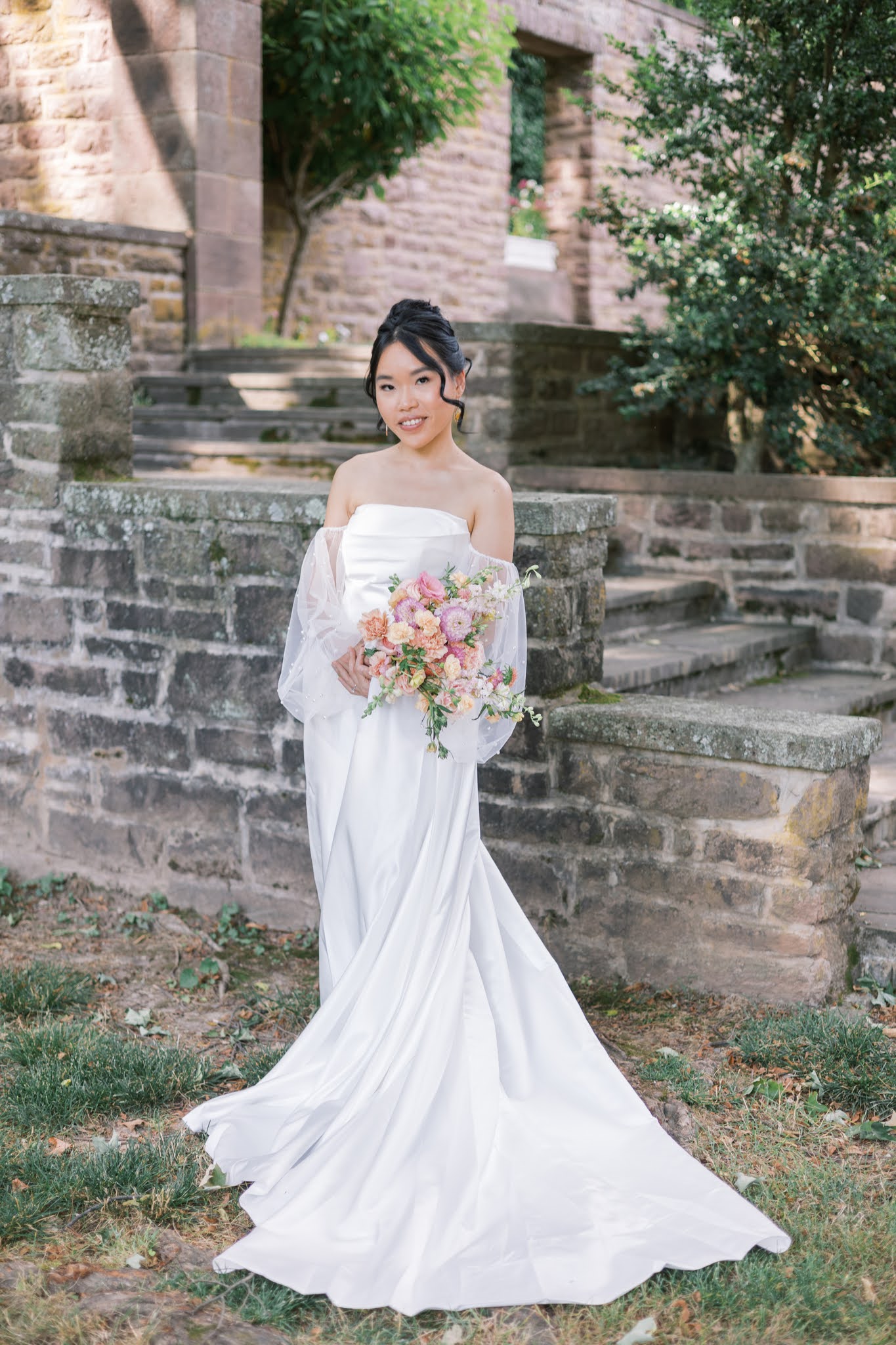 Bridal portrait, holding bouquet featuring soft summer garden florals in peach, pink, and greenery.