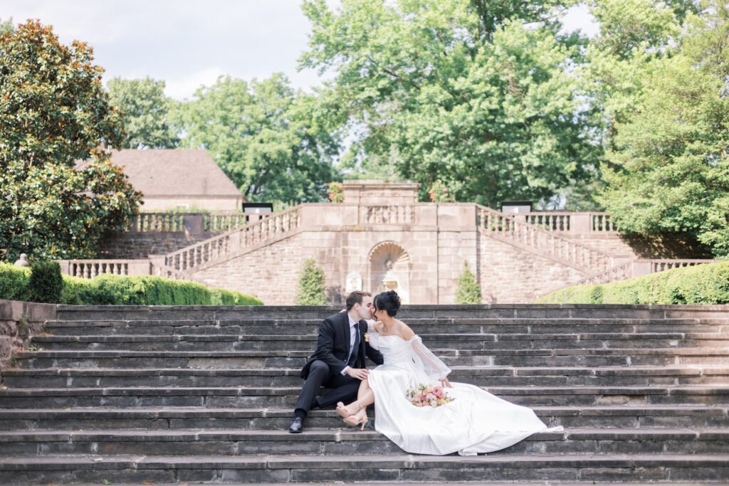 Couple kissing on their wedding day while sitting on the steps at Tyler Gardens