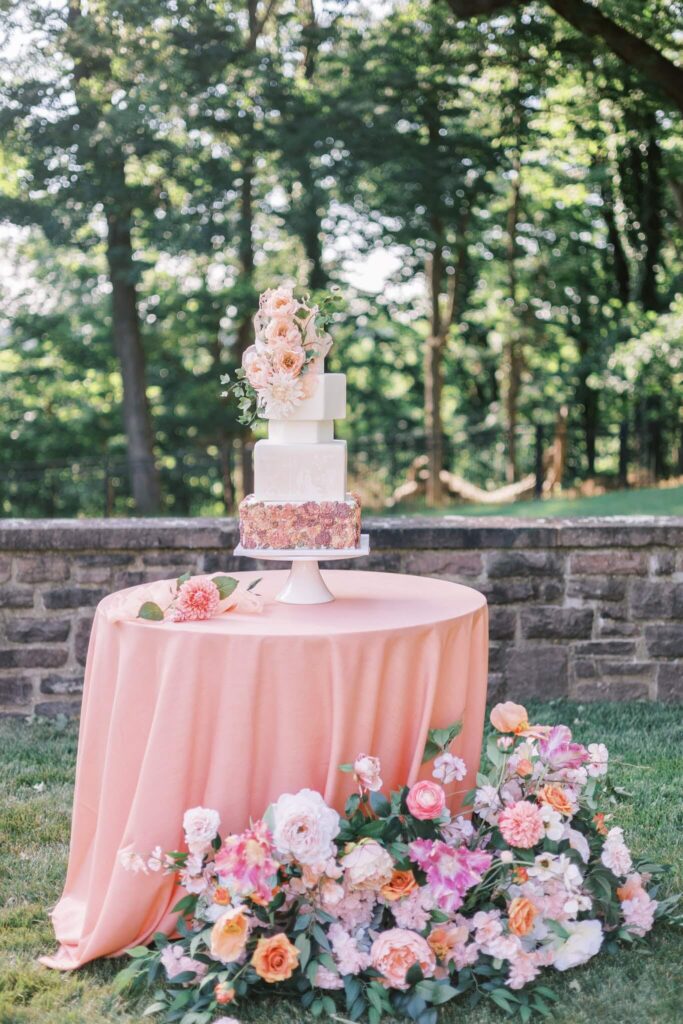 Wedding cake table with peach tablecloth and peach/pink floral arrangement