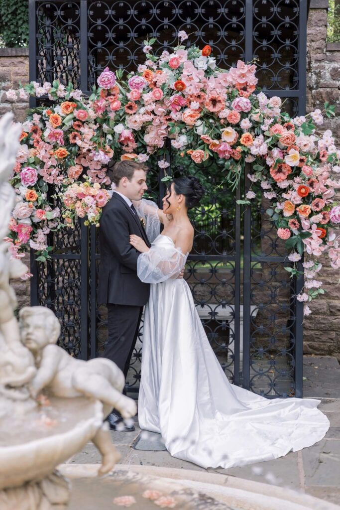 Portrait of bride and groom at Tyler Gardens, in front of a peach and pink floral arch