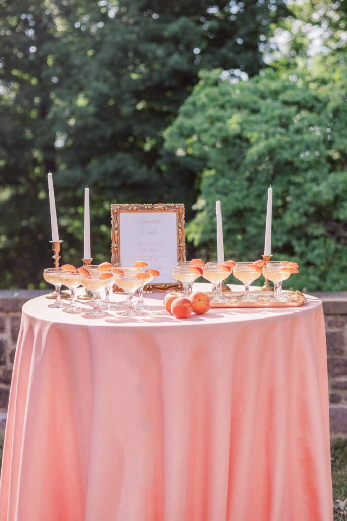 Drink table at summer garden wedding at Tyler Gardens. Pink tablecloth, peach drinks, and plenty of fresh peaches are featured as part of Pantone's color of the year, "Peach Fuzz."