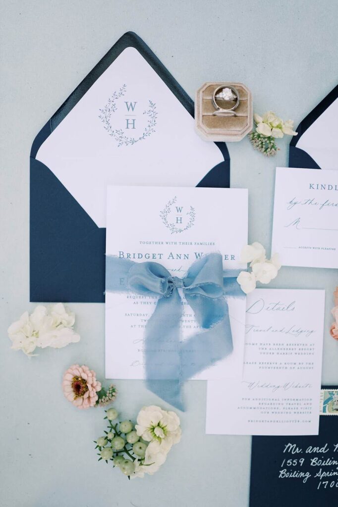 Wedding invitation suite featuring botanical monogram and blue bow