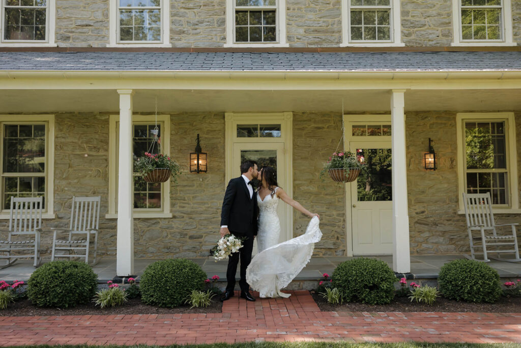 A bride and groom kiss on the porch of the farmhouse at The Farm at Eagles Ridge