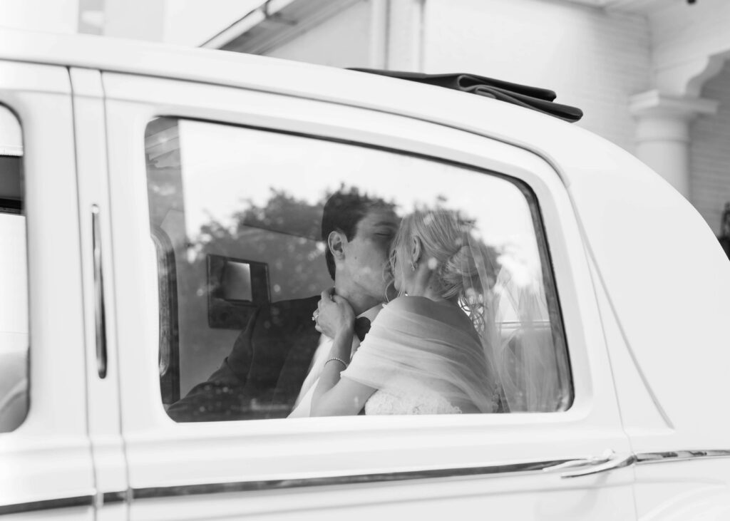 Bride and groom kissing in car driving away from wedding ceremony