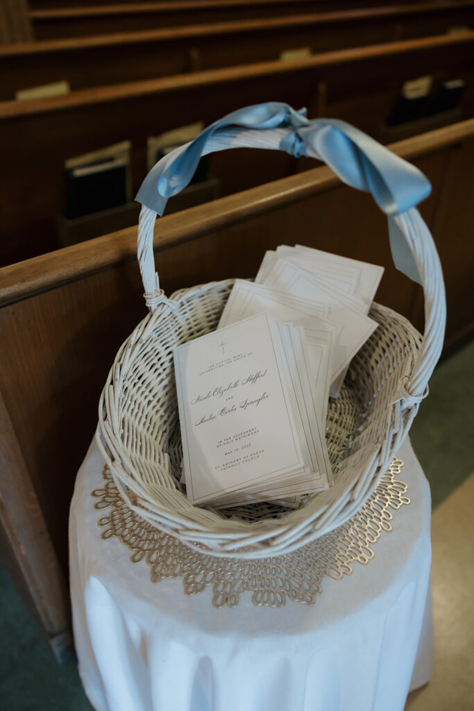 Basket of elegant wedding ceremony programs sits at the entrance of a church