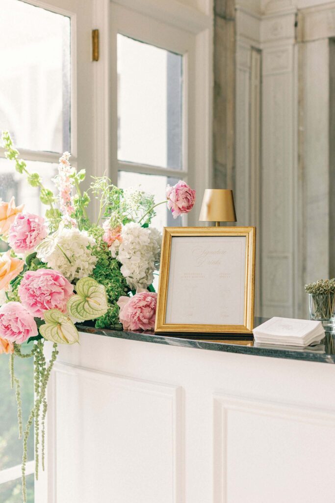 Signature cocktail sign in a gold frame surrounded by vibrant pink and green flowers