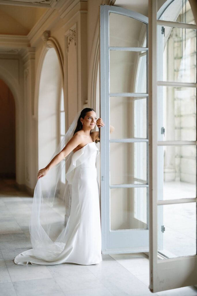 Bridal portrait in front of tall open doors with flowing veil