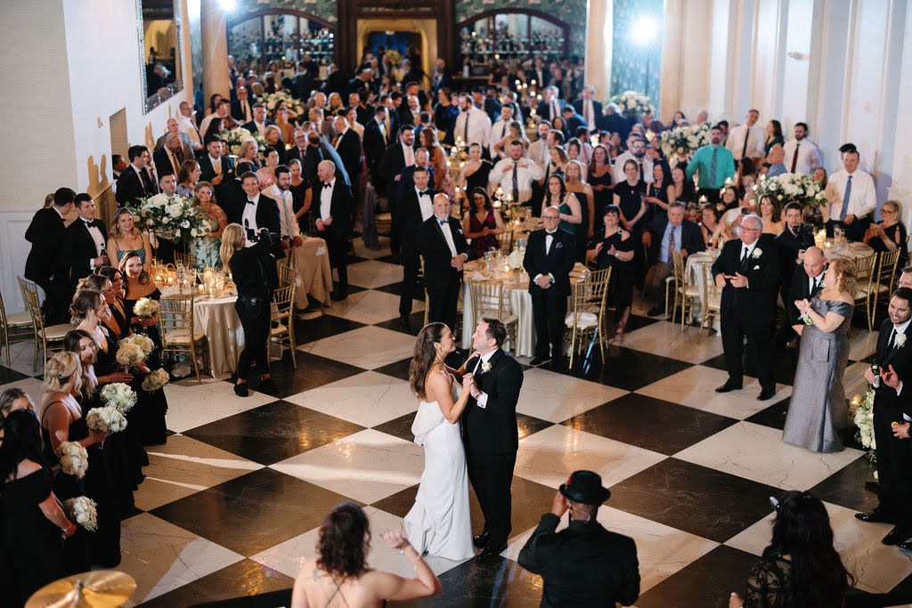 Wedding guests watch as bride and groom share first dance in grand ballroom
