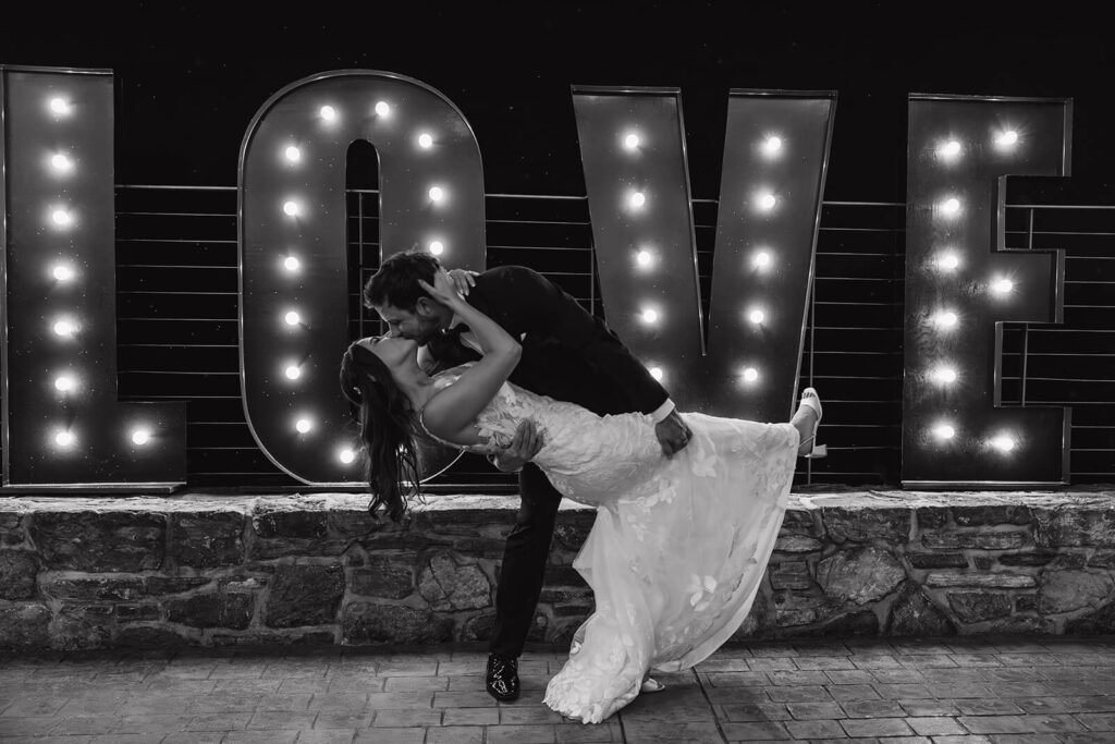 Bride and groom kiss in front of letters that spell LOVE