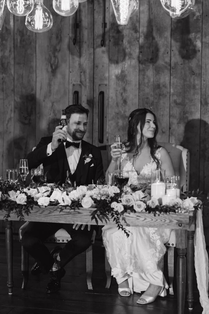 Bride and groom at sweetheart table toast their drinks