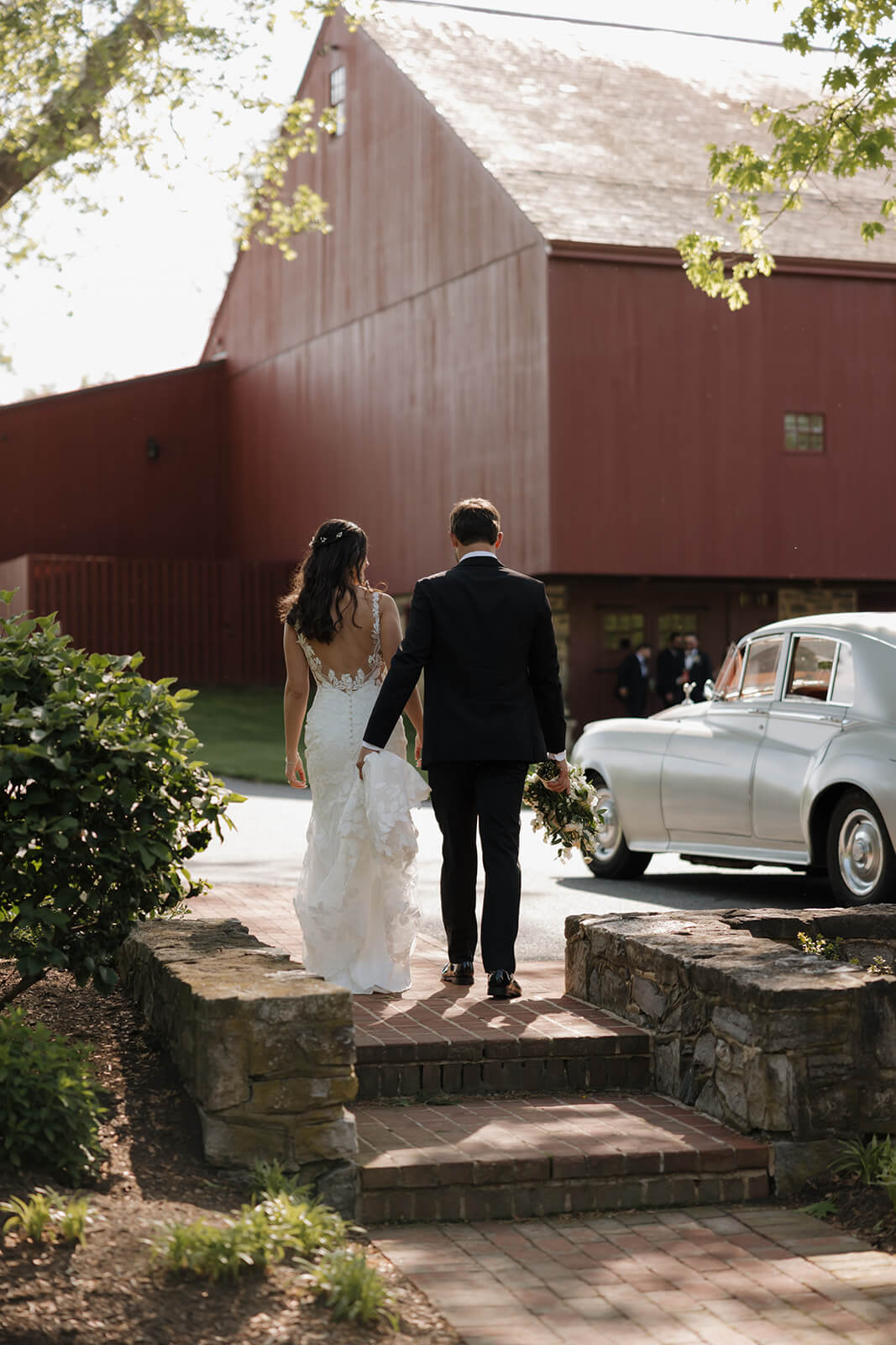 Bride and groom walk towards classic car in front of the barn at The Farm at Eagles Ridge