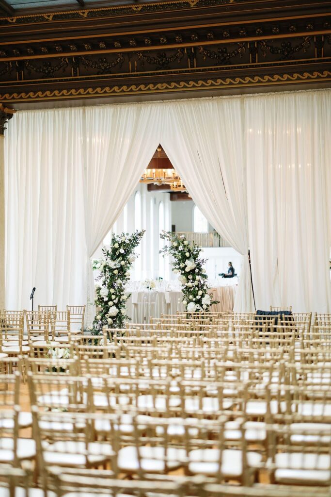 Wedding ceremony decorations, including deconstructed white and green arch and gold Chiavari chairs
