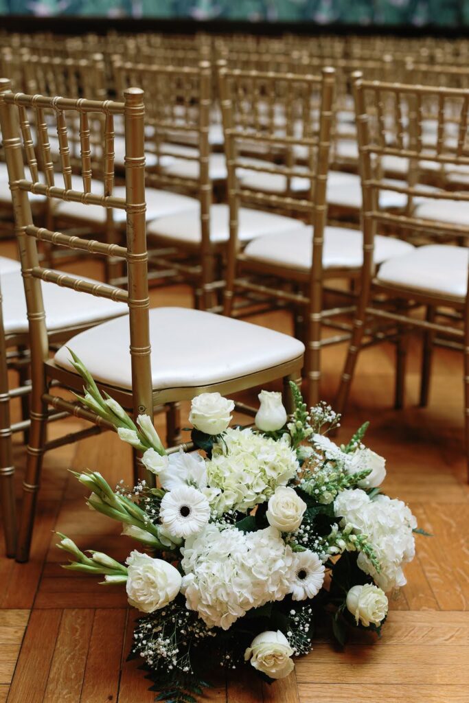 All white bouquet for wedding ceremony placed in aisle next to gold Chiavari chairs