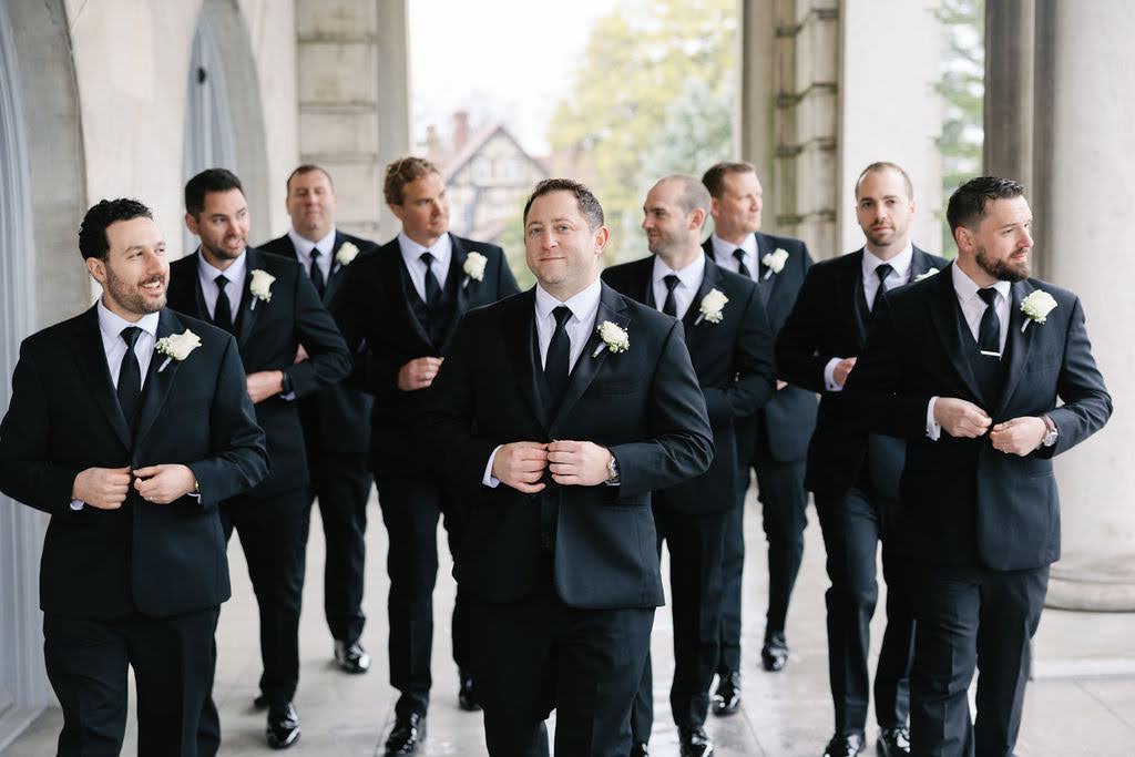 Groom walks with eight groomsmen behind him