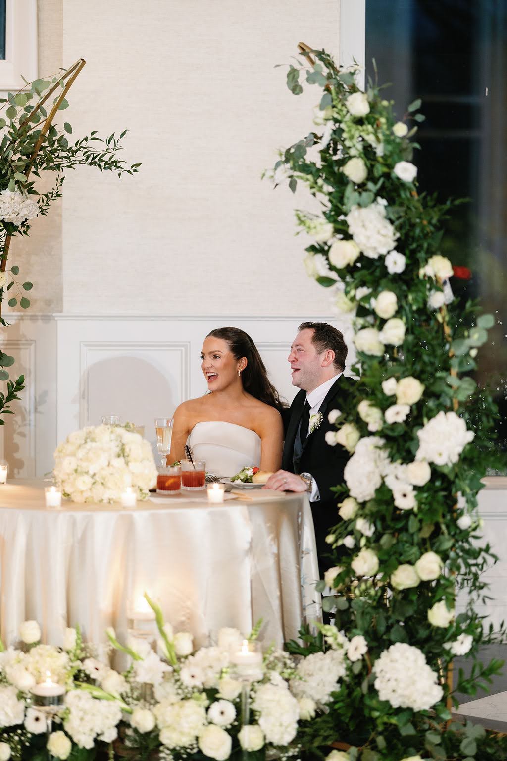 Bride and groom at sweetheart table react positively to wedding speeches
