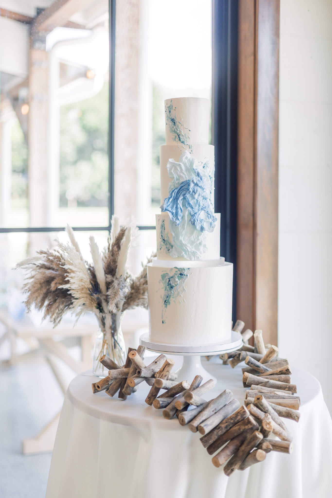 Four-tiered ocean wave inspired wedding cake on table with driftwood
