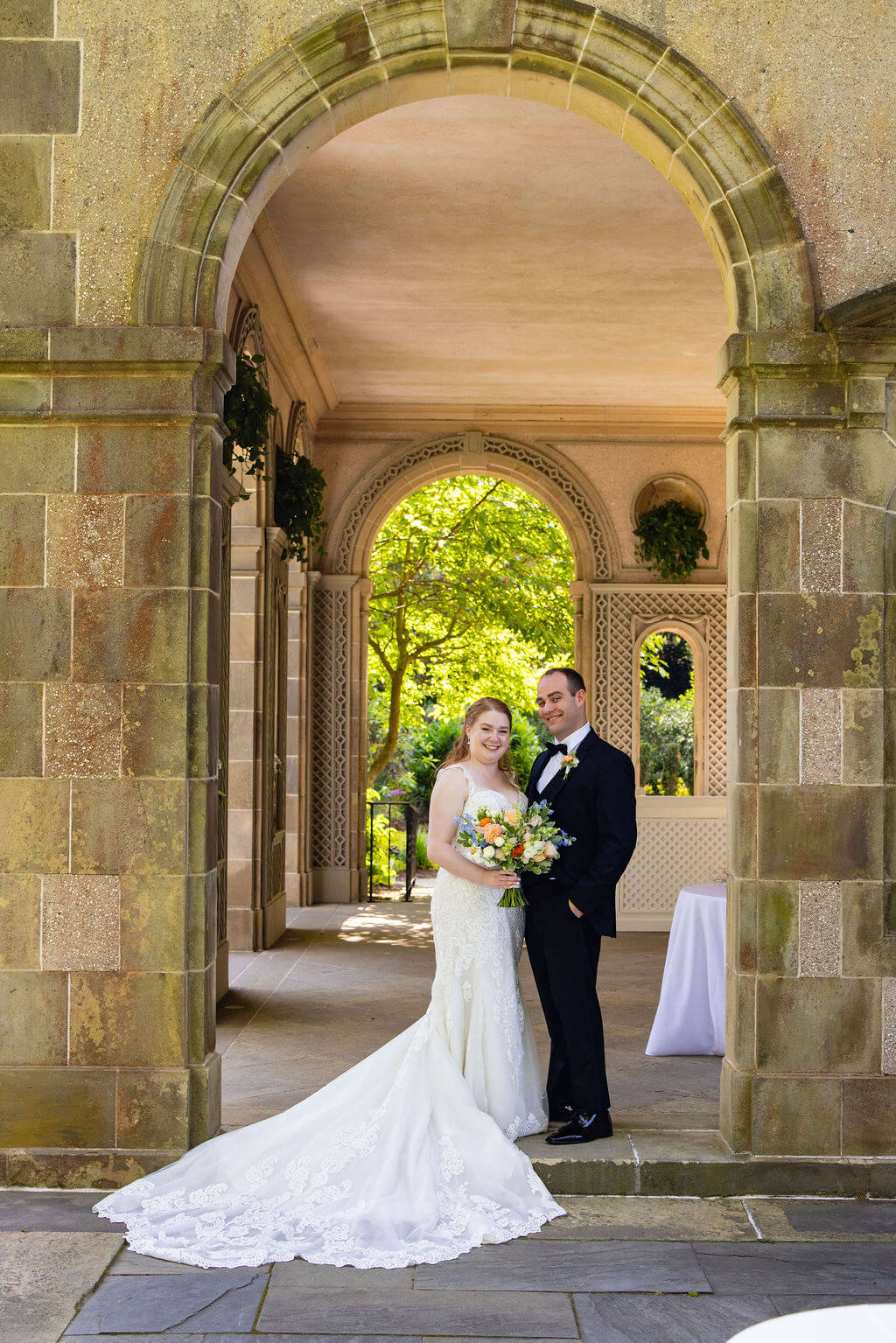 Bride and groom smile for a portrait beneath the arches at Glen Manor House