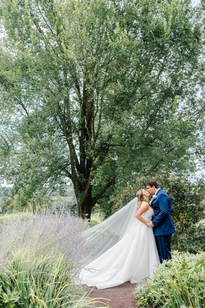 Bride and groom kissing outdoors in a garden, surrounded by lavender and trees