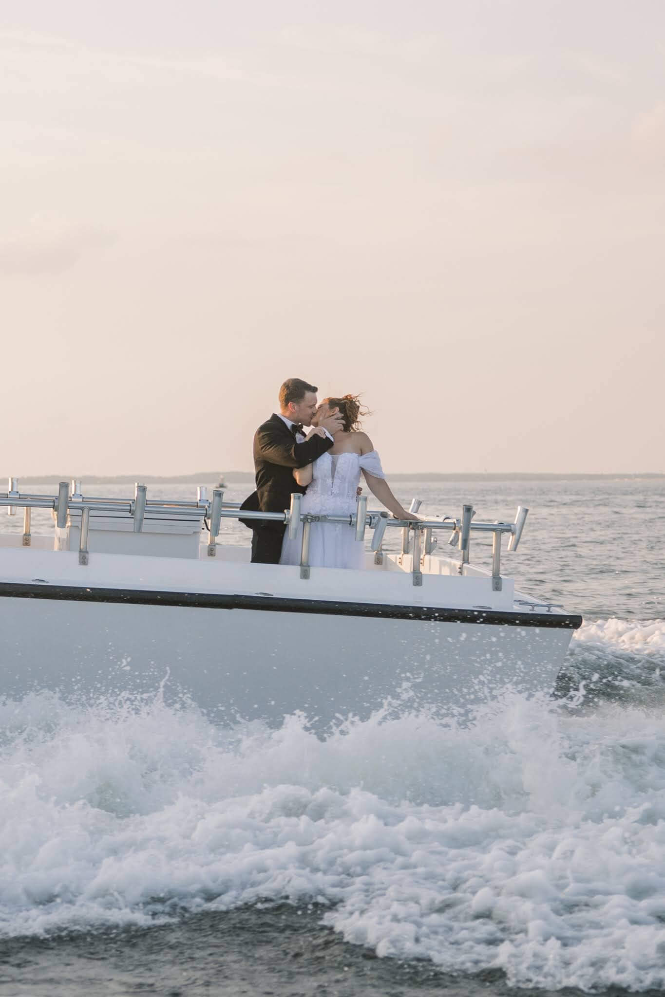Bride and groom kiss as the sun sets over the bay on the East Coast