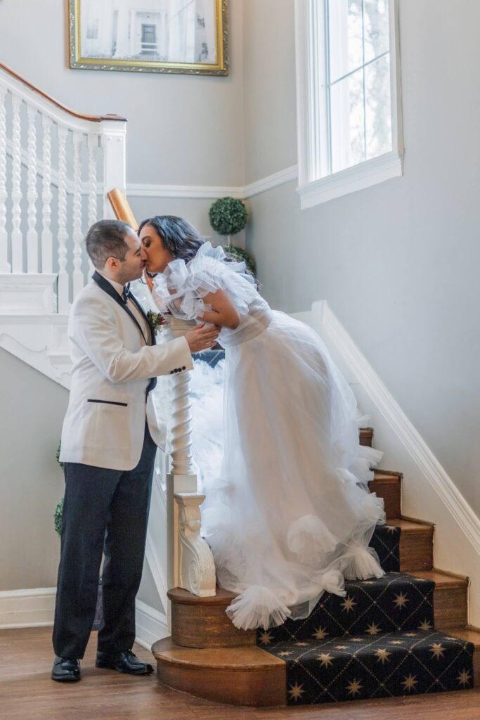 Bride and groom kiss on the staircase at Overhills Mansion