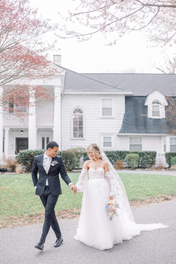 Bride and groom walk hand in hand in front of Overhills Mansion, an East Coast wedding venue