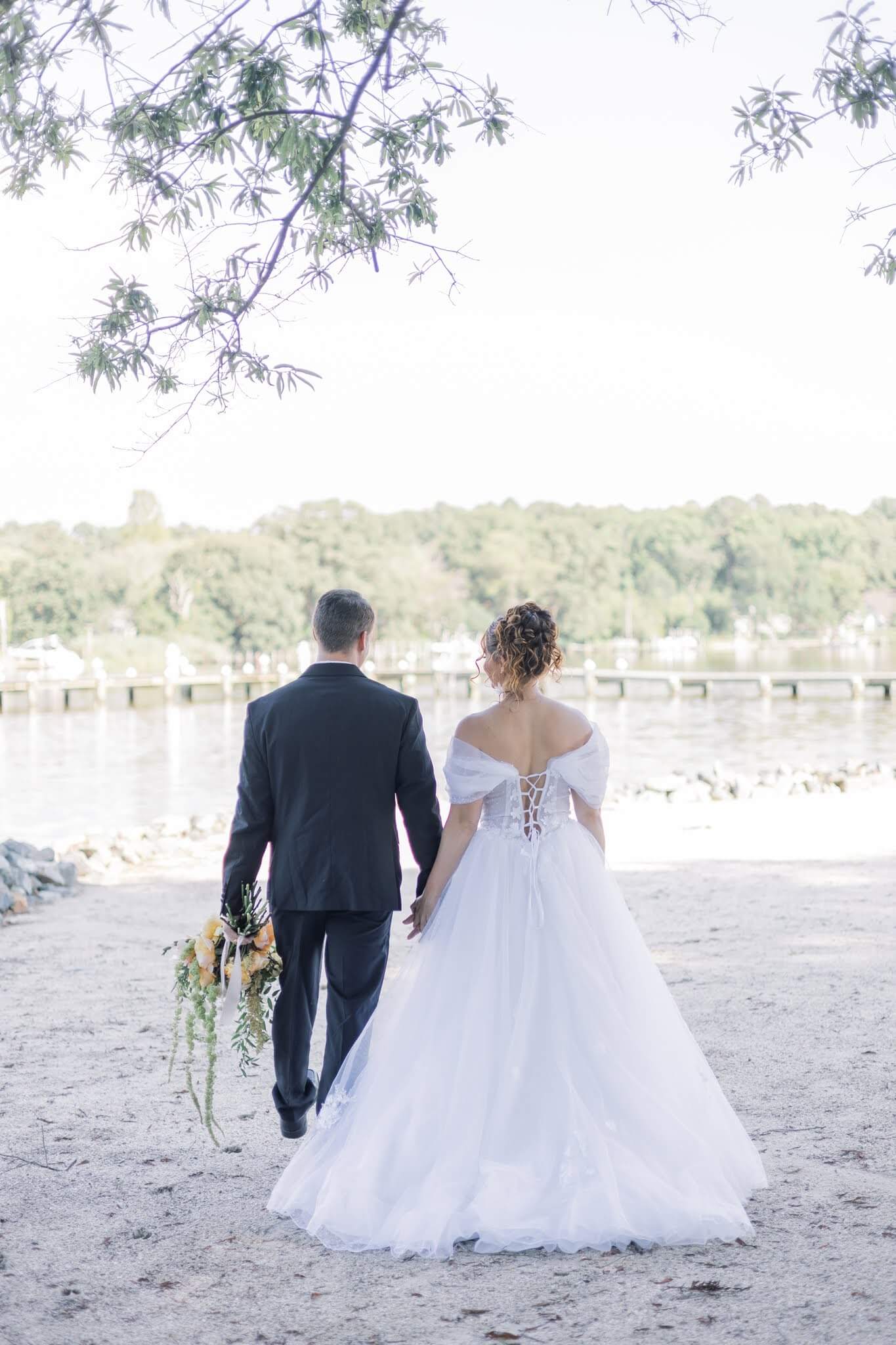 Bride and groom walk hand in hand on the shore of the Chesapeake Bay