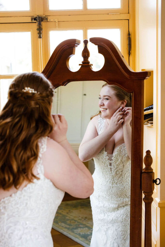 Bride puts on earrings while looking in mirror on her wedding day