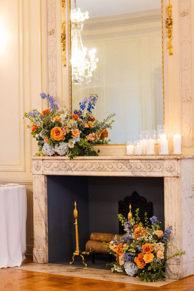 Colorful floral arrangements and white pillar candles adorn a fireplace mantel