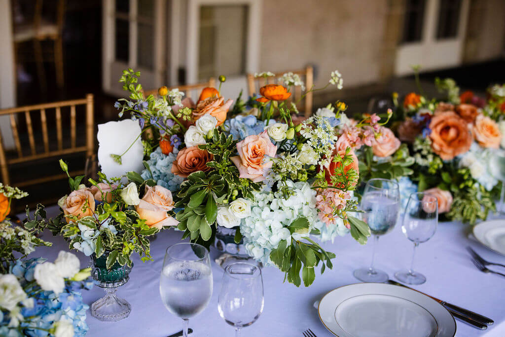 Colorful floral arrangement of roses, hydrangeas, and delphinium sit atop a purple tablecloth