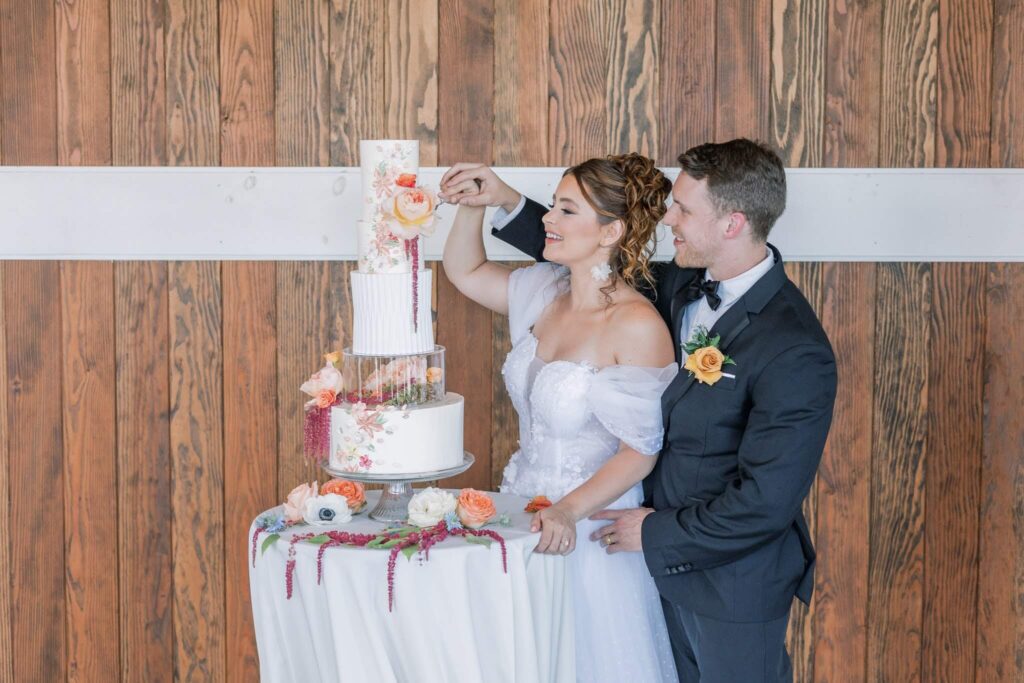 Bride and groom cut their five-tier wedding cake featuring orange floral details