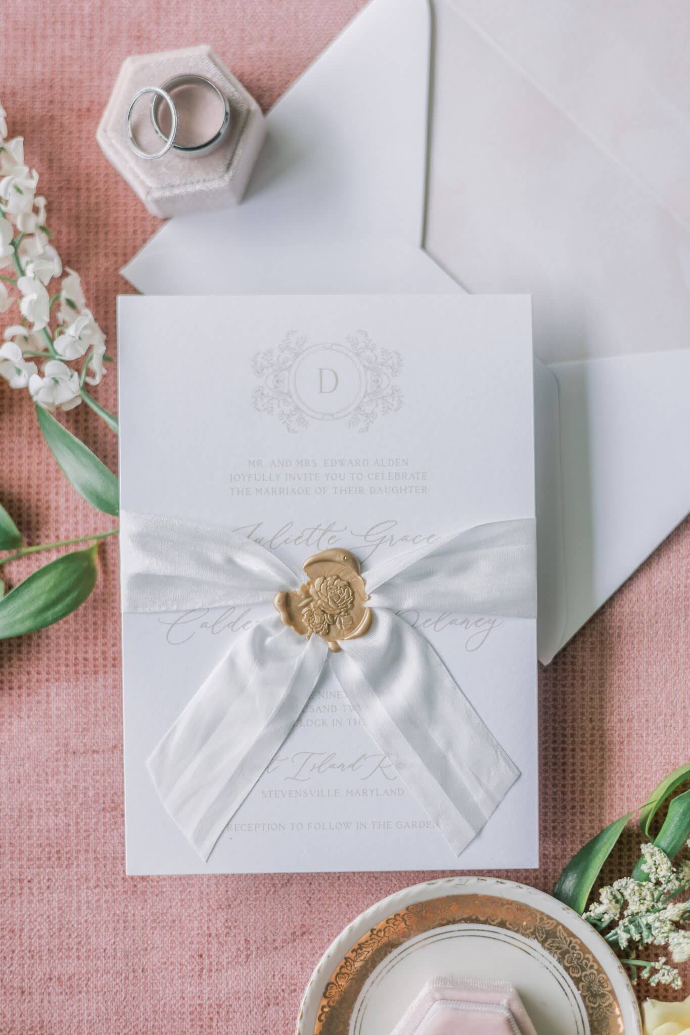 White silk ribbon and gold wax seal with a rose enclosing a wedding invitation 