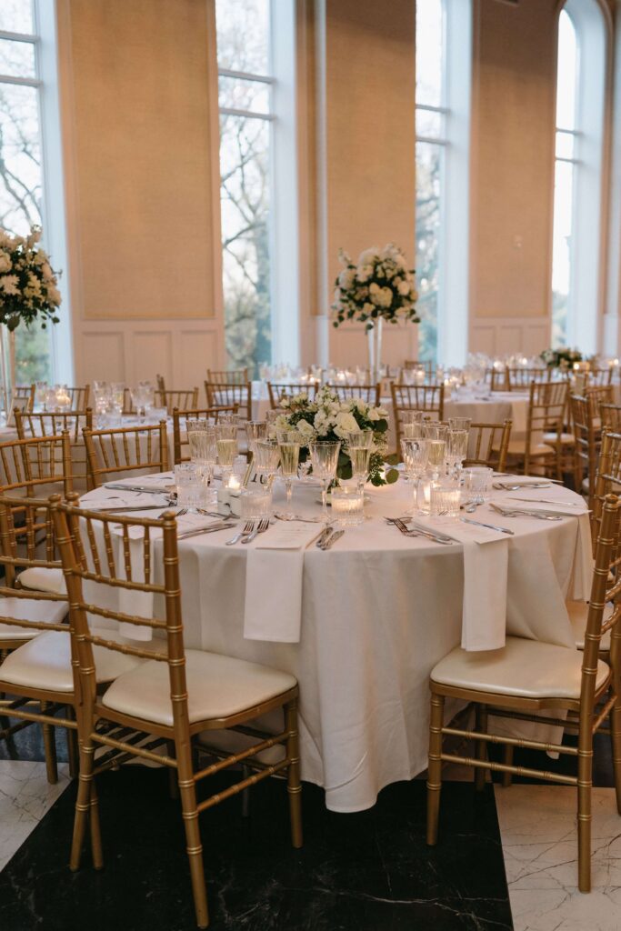 Romantic wedding reception table with white tablecloths, white roses, and gold Chiavari chairs