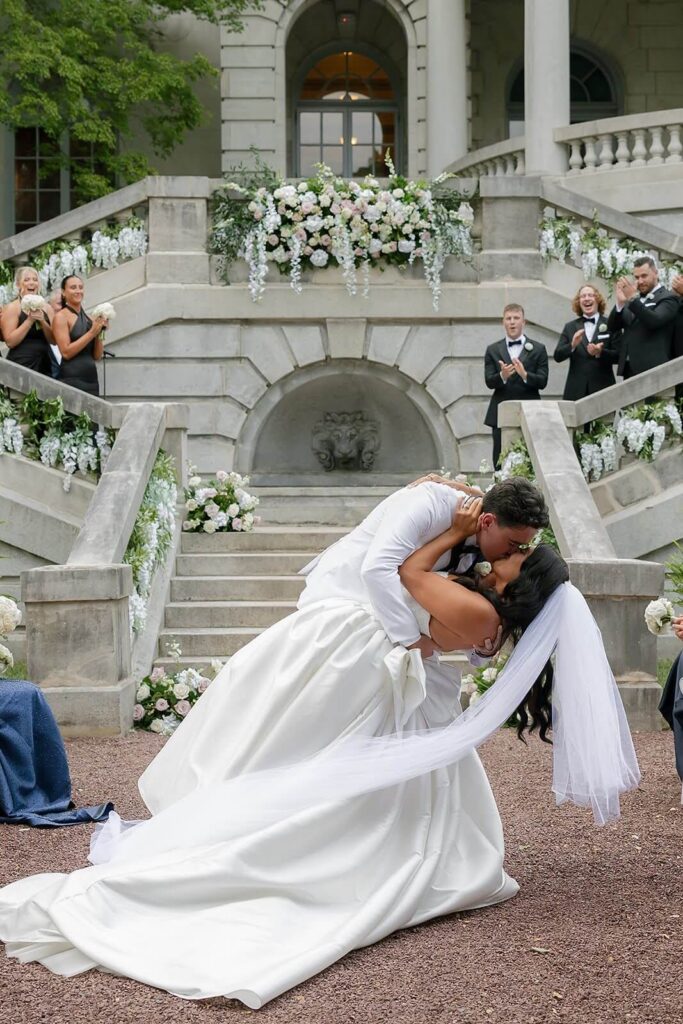 Bride and groom share a kiss after their wedding ceremony as guests cheer