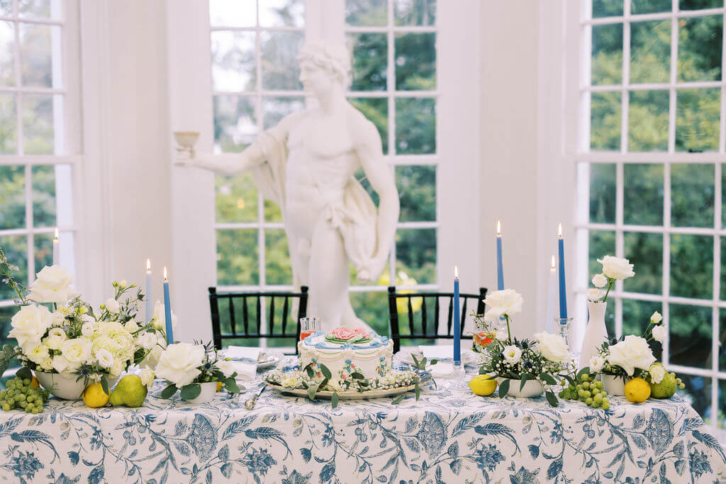 Vintage-inspired wedding reception table with blue candles, white flowers, pears and lemons used as decorations, and a white marble sculpture