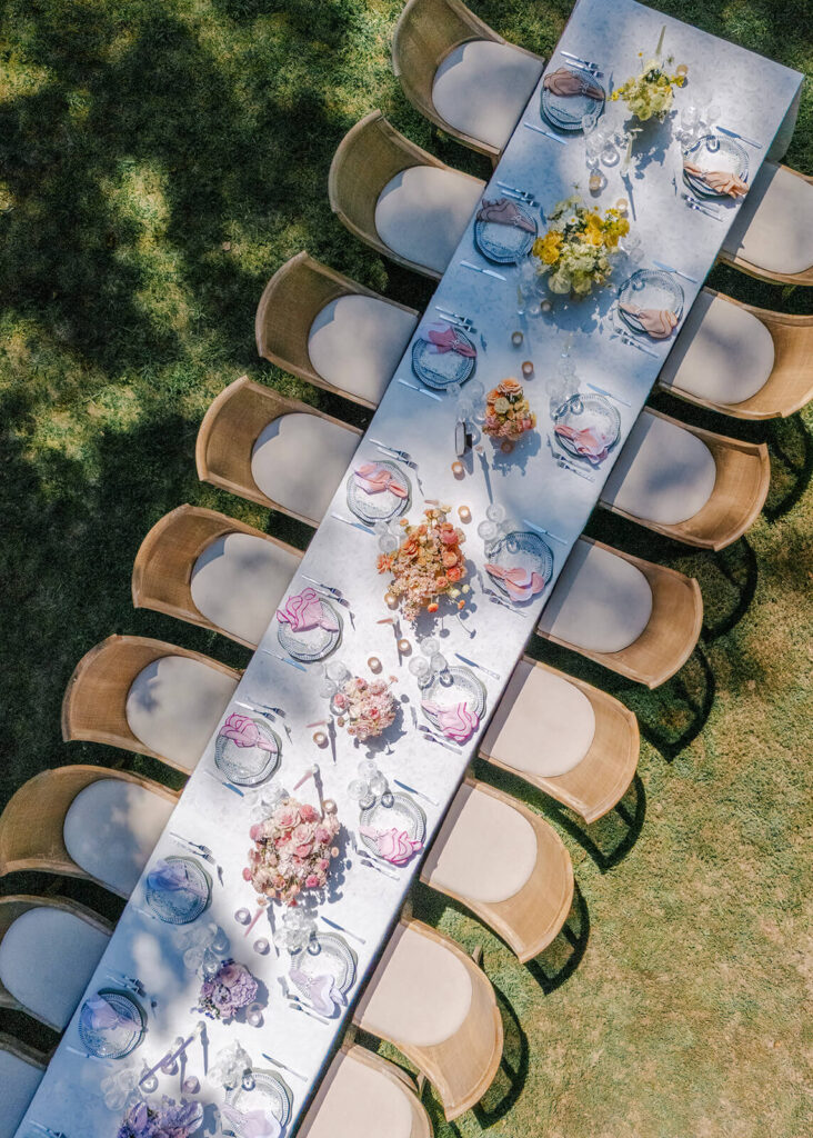 A long wedding reception table outdoors with rainbow colored florals