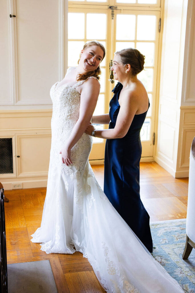 Mother of the bride helps bride put on her wedding dress