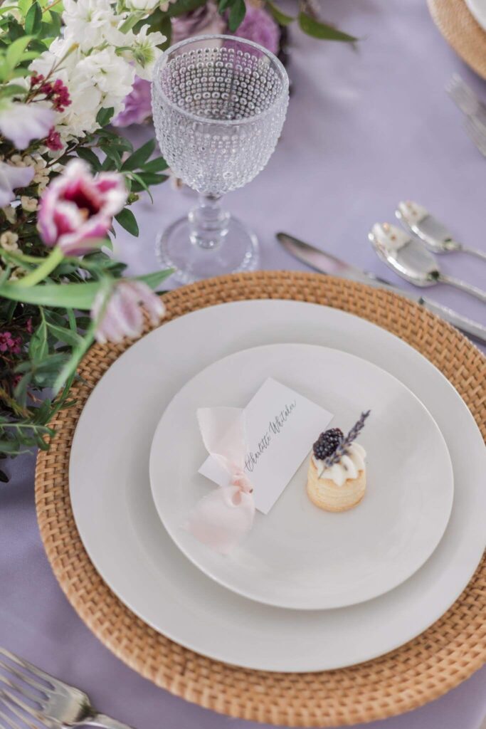 Wedding reception place card with light pink silk ribbon sits on a plate with dessert