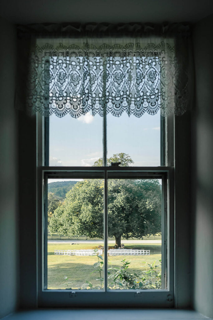 Looking through a window at an outdoor wedding ceremony set up under a large tree