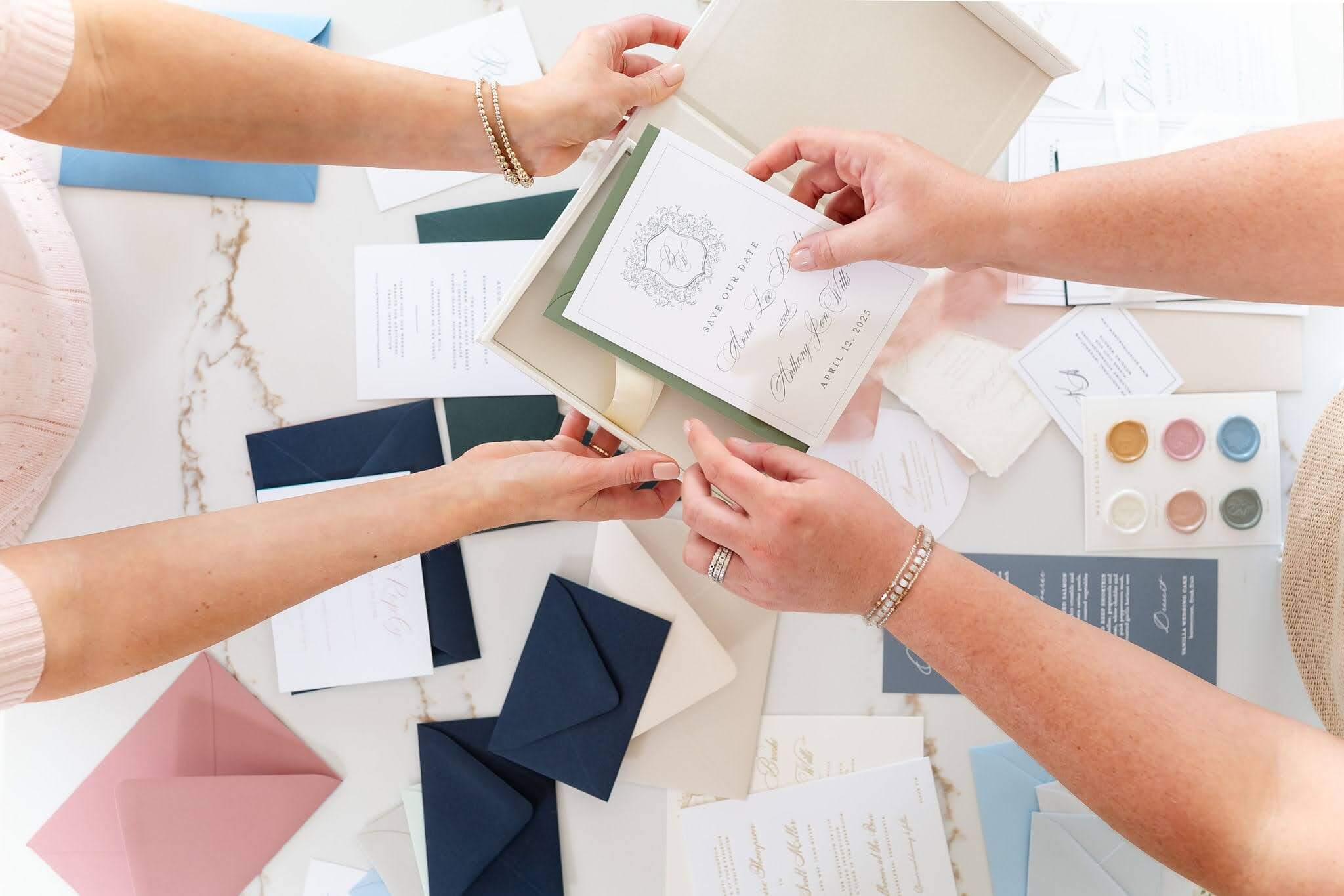 A wedding stationer places a save the date card into a linen keepsake box for one of their custom invitation couples