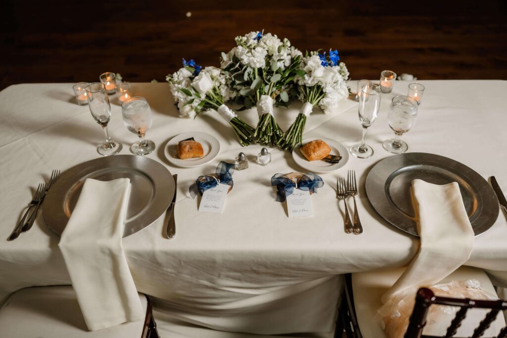 Wedding reception sweetheart table in tones of ivory, green, and sapphire