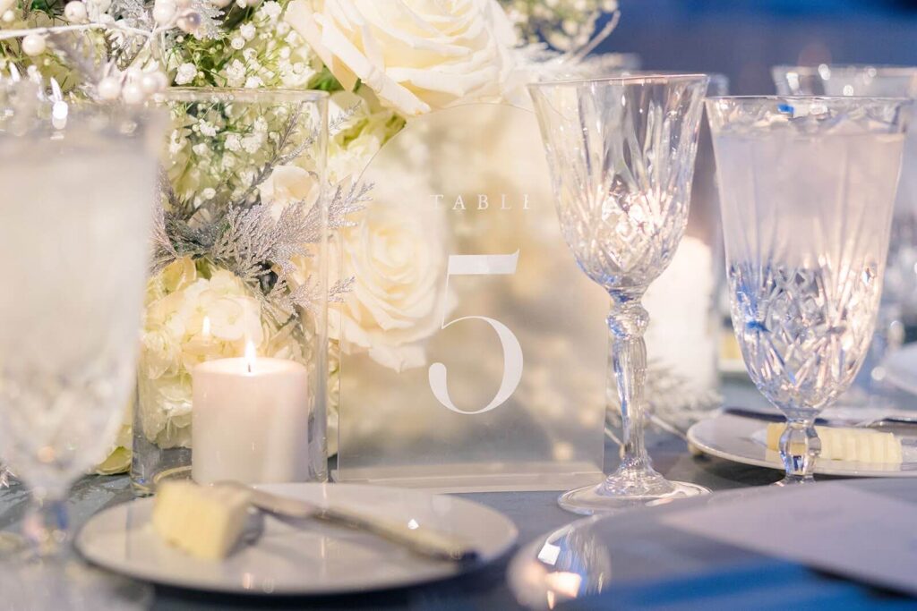 Close up of the winter gala table featuring an acrylic table number display, candles, and crystal drinkware