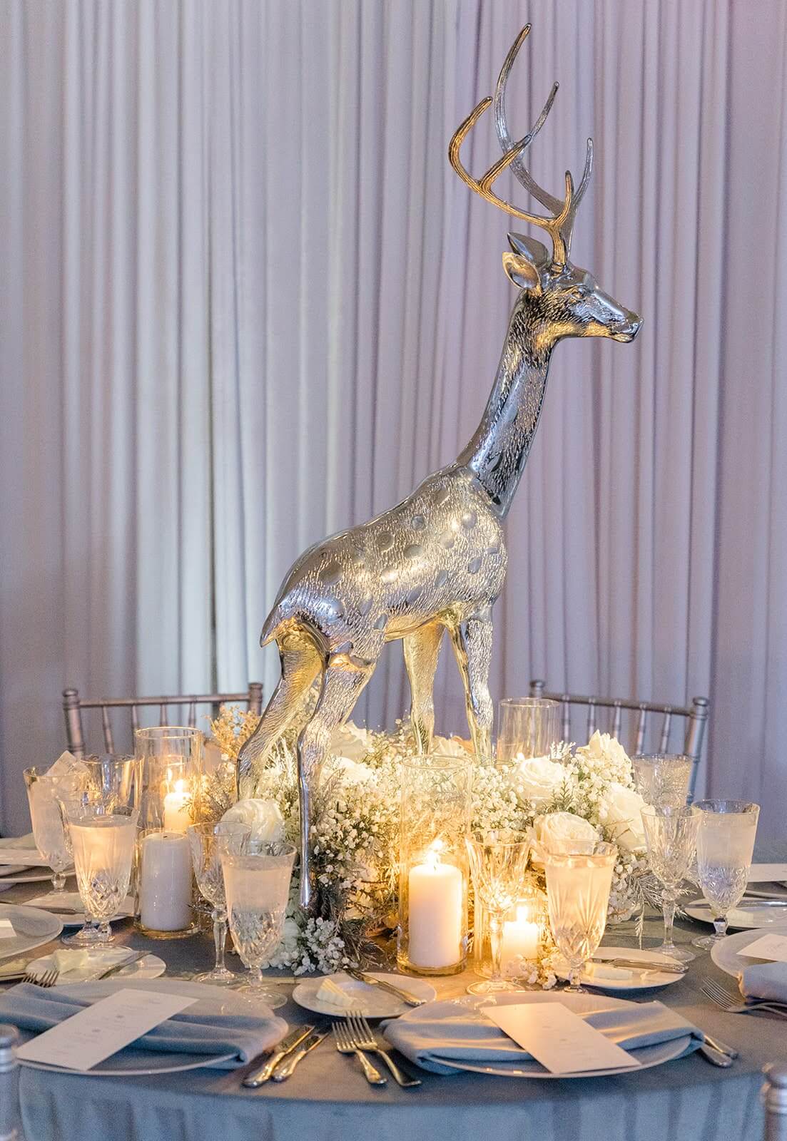 Elegant winter themed tablescape with silver deer sculpture and menu cards atop icy blue place settings