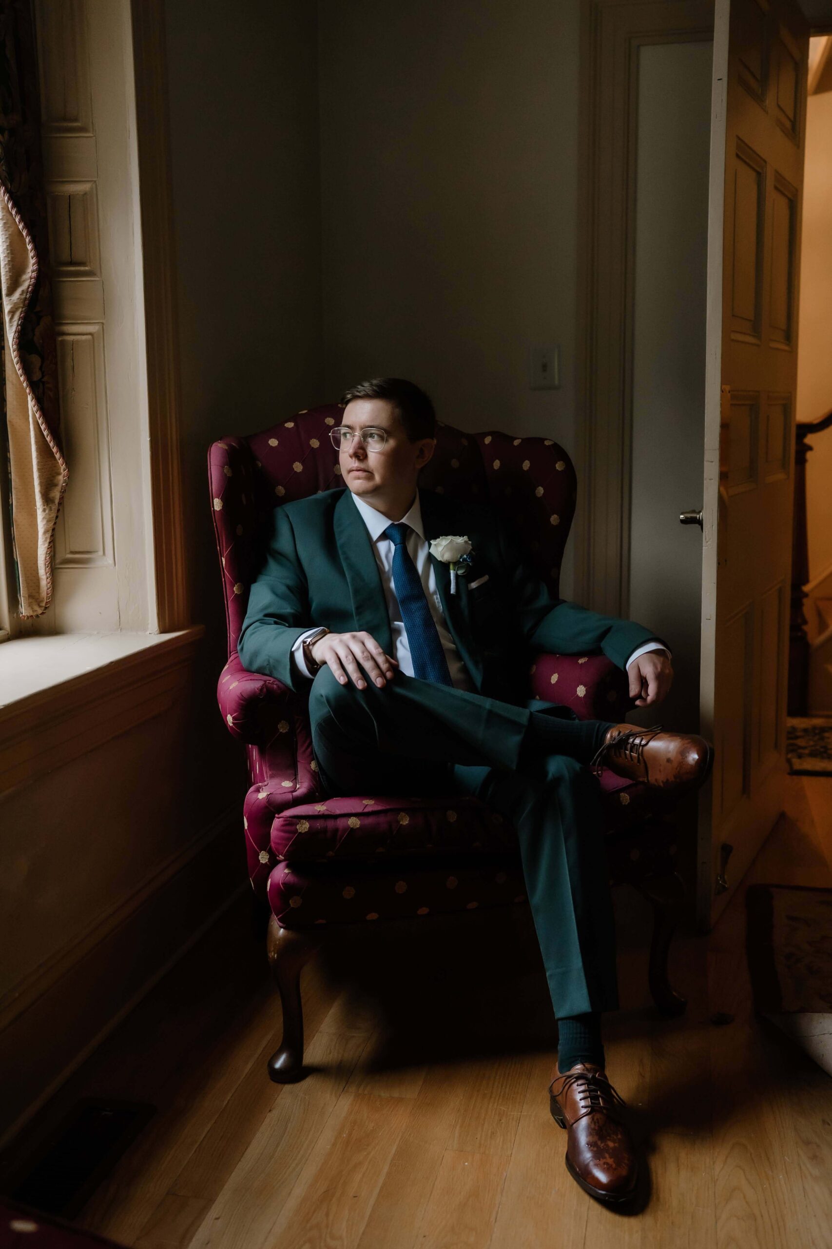 Portrait of the groom looking out the window on his wedding day at Joseph Ambler Inn