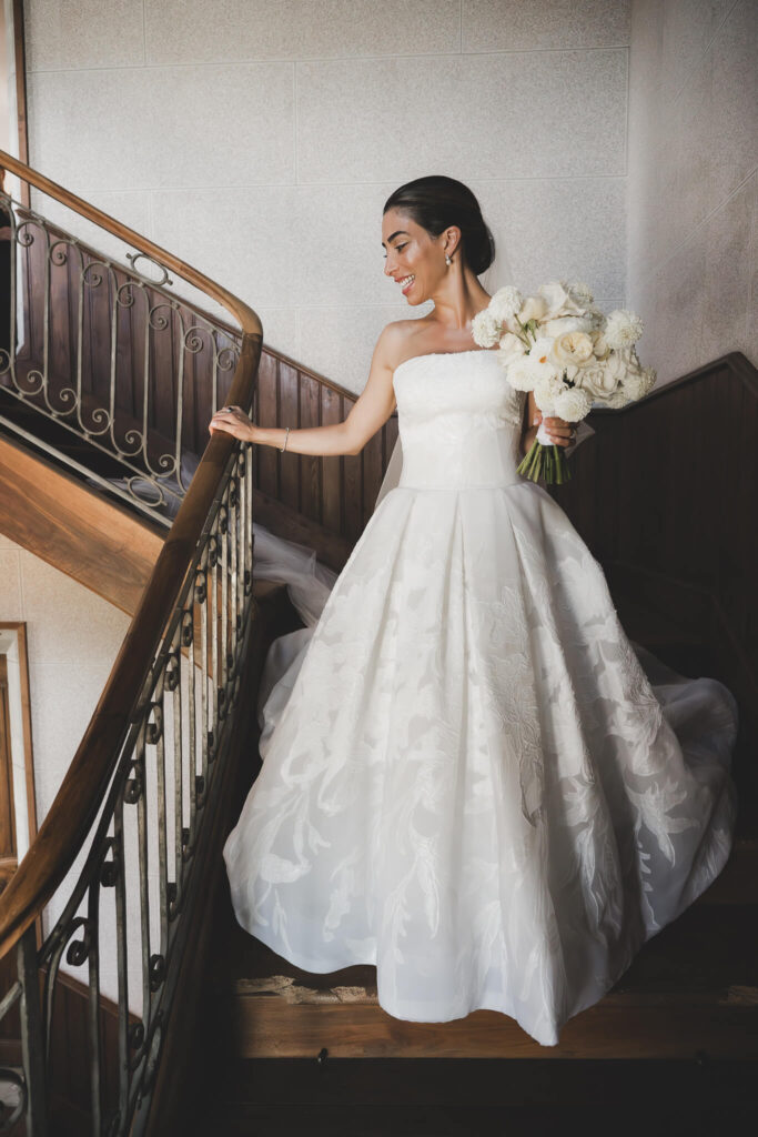 Bride smiling and descending staircase with her wedding bouquet
