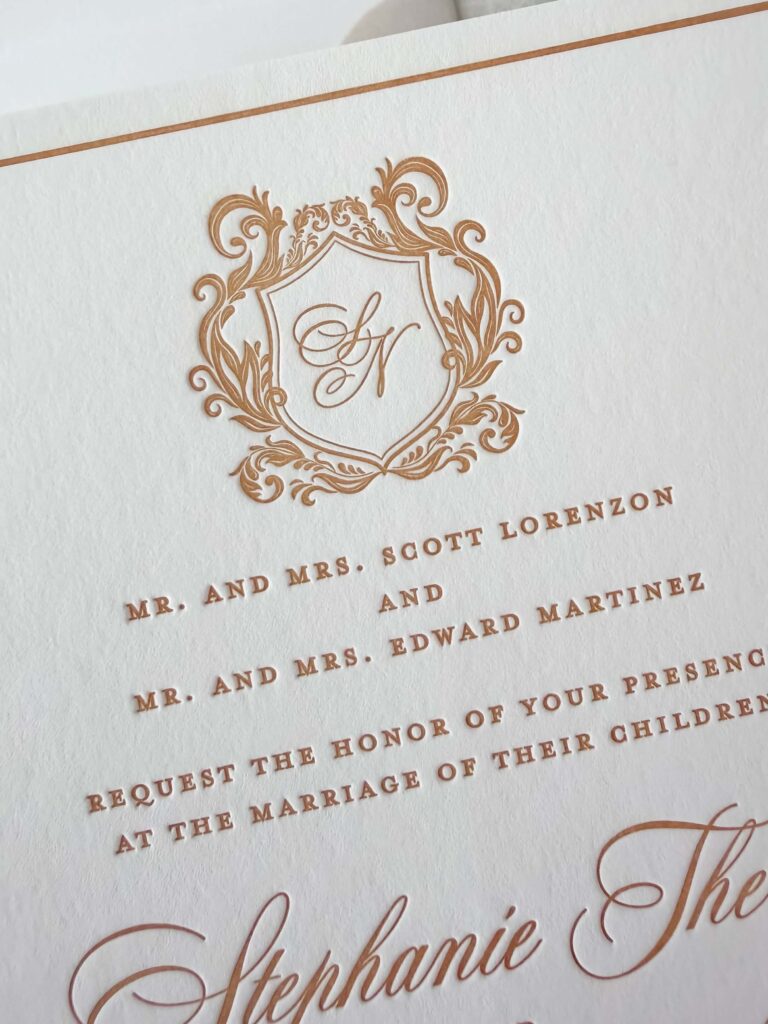 Formal wedding invitation closeup featuring custom crest and monogram in gold letterpress printing