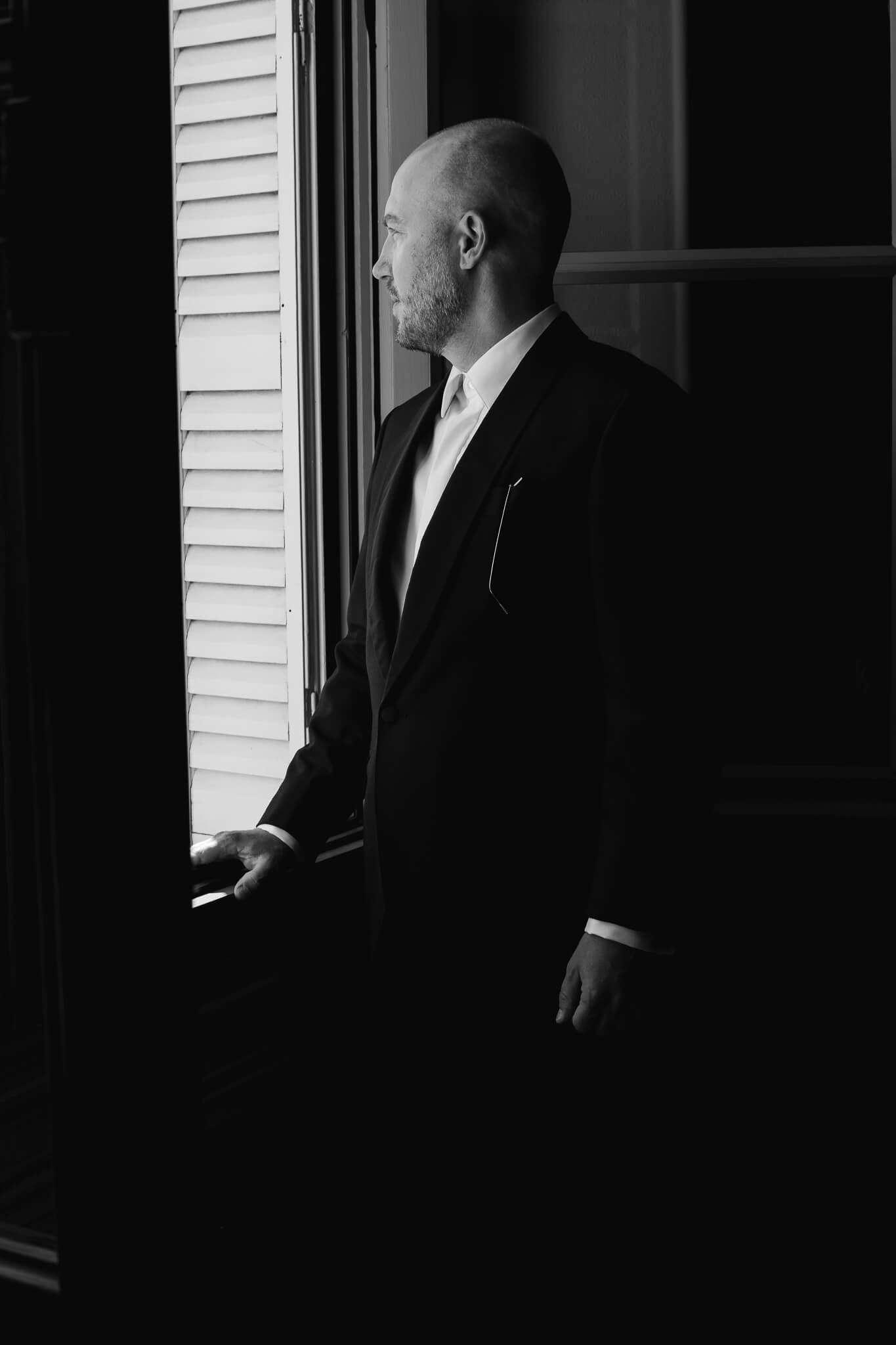 Thoughtful portrait of groom looking out the window on his wedding day
